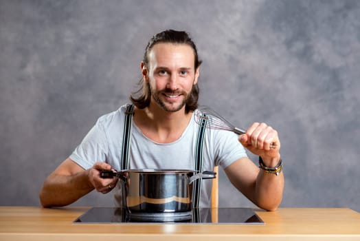 young bearded man with cooking pot in front of gray background