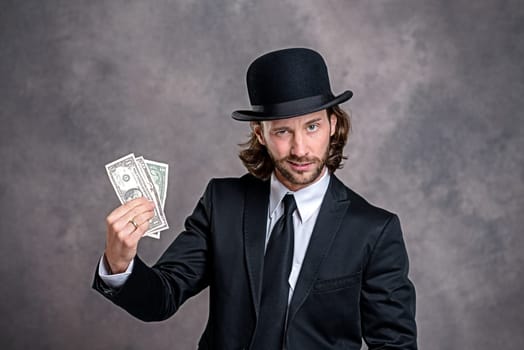 young businessman with bowler hat in black suit showing money