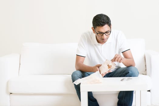 Lonely young single Asian Indian man eating food alone at home, copy space at side. Having nasi lemak as lunch.