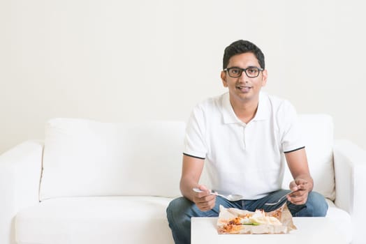 Young single Indian man eating food alone, copy space at side. Having nasi lemak as lunch. Lifestyle of Asian guy at home.