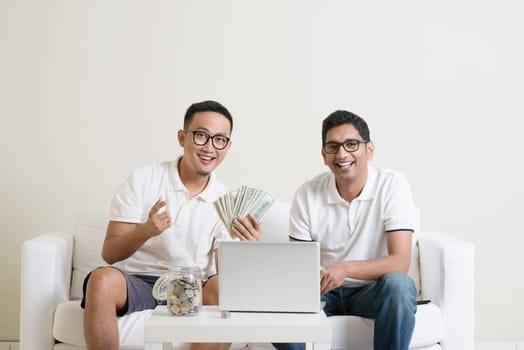 eBusiness concept. Young guys counting cash with partner, earning money from their successful online business. Asian men working from home.