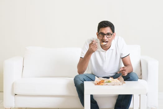 Lonely young single Indian man eating food alone, copy space at side. Having nasi lemak as lunch. Lifestyle of Asian guy at home.