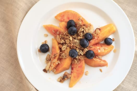 Plate of fresh blueberries and peaches, topped with granola, shot from overhead