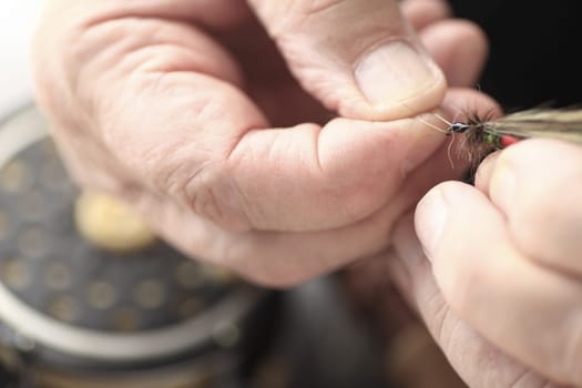 Closeup view of a man holding an imitation insect artificial fly, fishing reel in background