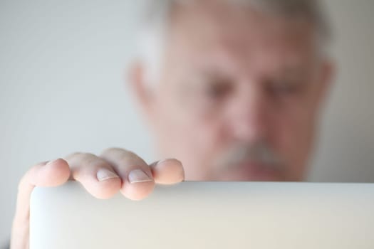 Older man has hand on his laptop, face defocused