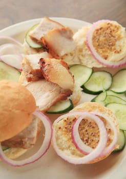 Sliced roast pork belly with cucumber and onion slices on rolls spread with whole-grain mustard