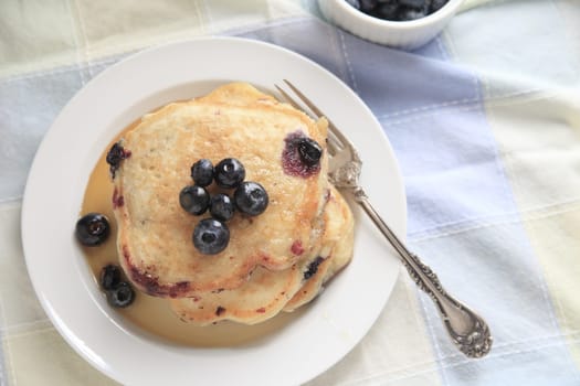 Freshly made pancakes with blueberries and syrup on a plate with fork, copy space included