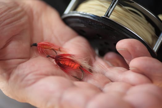 Fisherman holds two similar fly fishing lures next to his reel.