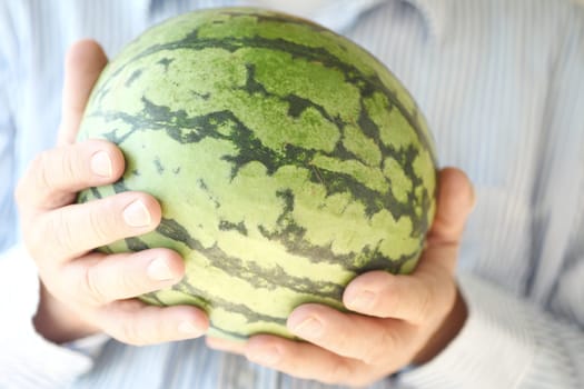 A man holding a small watermelon with both hands