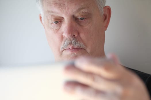 A senior man with a hand on his laptop cover checks his screen.