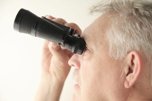 Senior man looking upward with an old pair of binoculars, copy space included.
