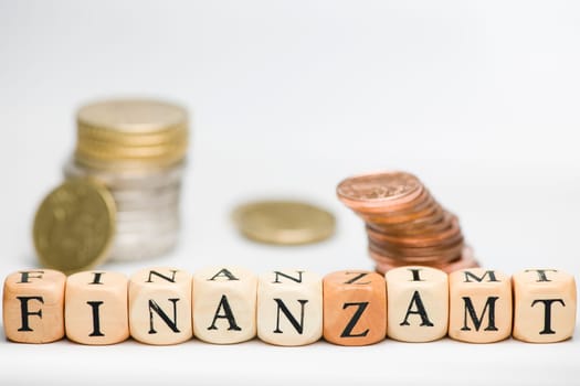 A series of letter cubes representing the word "TAX OFFICE"" with small fuzzy stacked coin on white background"