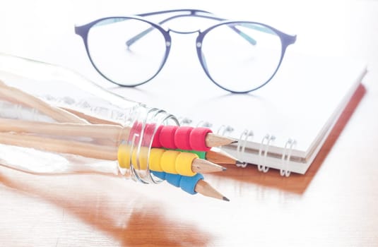 Pencils in bottle with eyeglasses on notebook, stock photo
