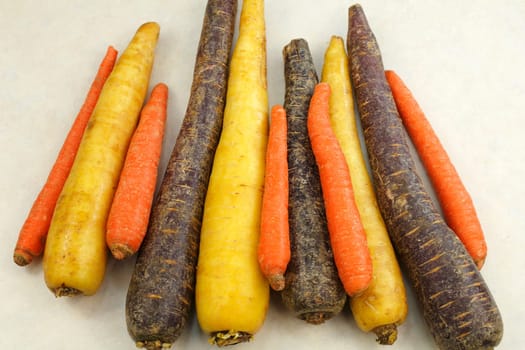 Ingredient mix of whole, raw orange, yellow and purple carrots on a beige countertop.  Three different colors of organic whole raw carrots on a kitchen counter top
