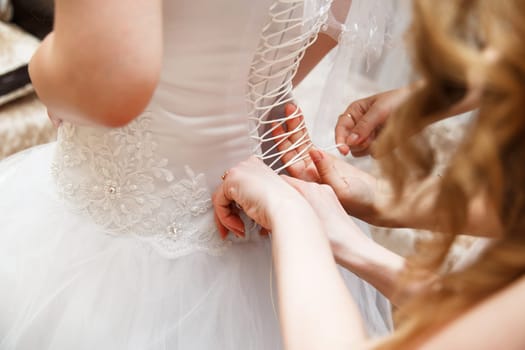 Bridesmaid is helping the bride to dress
