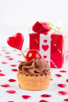 Cupcake with cherry in front of gift box on white wooden background. Valentines day concept.