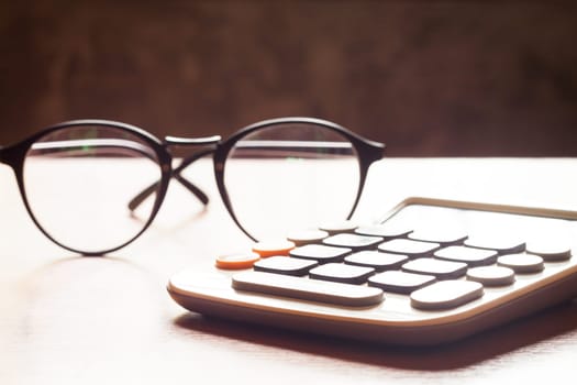 Calculator with eyeglasses on wooden table, stock photo