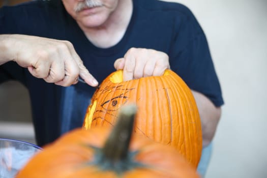 Guided by his sketch, an older man carves a jack o' lantern.