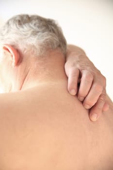 A senior man tries to reach a spot in the middle of his back.