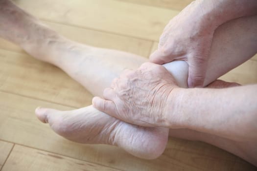 Senior man seated on floor holds an ankle with both hands.