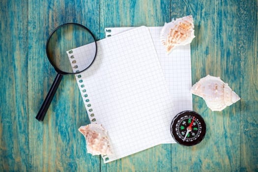 Paper sheets,seashells, compass and magnifying glass on wooden background