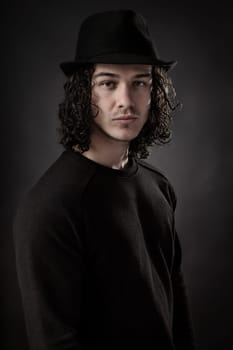 Portrait of young man dressed in black with long hair and hat