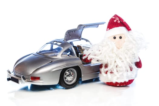 Santa Claus or Father Frost with old vintage automobile on white background with reflection. Main focus of image on Santa Claus and selective on turned the back side and opened right door toy retro car