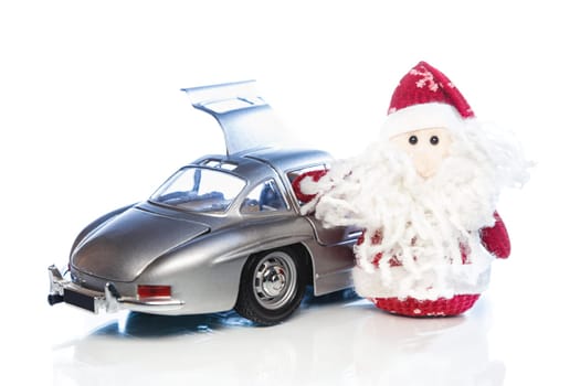 Santa Claus or Father Frost with old vintage automobile on white background with reflection. Main focus of image on Santa Claus and selective on turned the back side and opened left door toy retro car