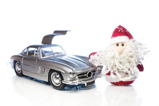 Santa Claus or Father Frost with old vintage automobile on white background with reflection. Main focus of image on Santa Claus and selective on turned right and opened door toy retro car