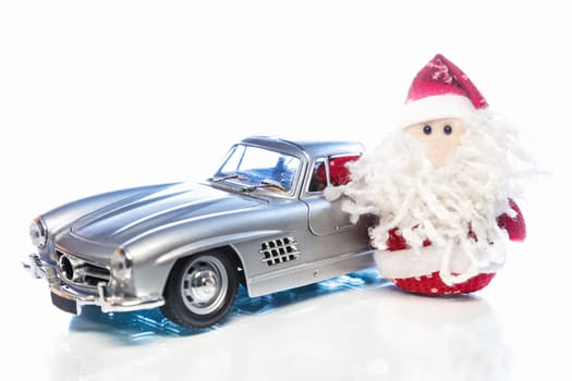 Santa Claus or Father Frost with old vintage automobile on white background with reflection. Main focus of image on Santa Claus and selective on turned left toy retro car