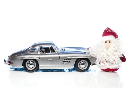 Santa Claus or Father Frost with old vintage automobile on white background with reflection. Main focus of image on Santa Claus and selective on the side turned toy retro car