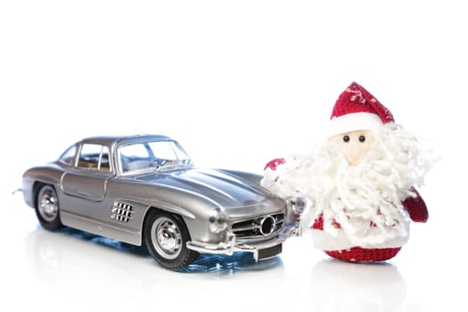 Santa Claus or Father Frost with old vintage automobile on white background with reflection. Main focus of image on Santa Claus and selective on turned right toy retro car