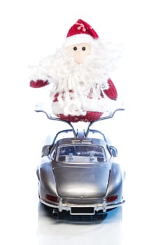 Santa Claus or Father Frost stands on opened doors of old vintage automobile on white background with reflection. Main focus of image on Santa Claus and selective on turned the back side toy retro car