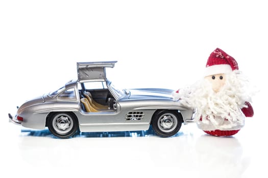 Santa Claus or Father Frost with old vintage automobile on white background with reflection. Main focus of image on Santa Claus and selective on the side turned and opened doors toy retro car