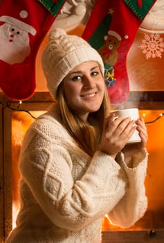 Closeup portrait of beautiful woman in woolen sweater drinking tea at fireplace