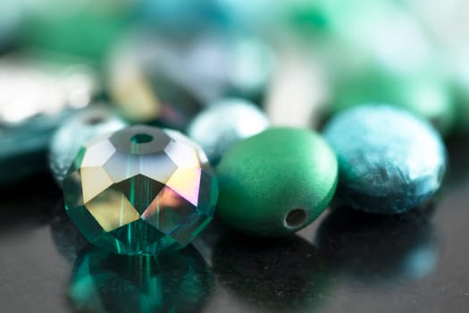 Crystal and glass coated beads with green and teal hues, on dark surface.