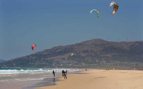 Sportsmen kite surfers on clean beach in summer day, Tarifa, Spain