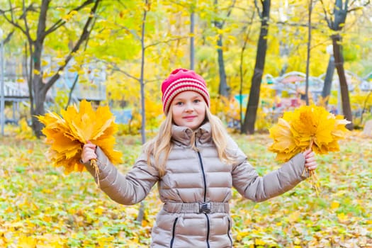 Photo of playing girl with two bouquets of sheets in autumn