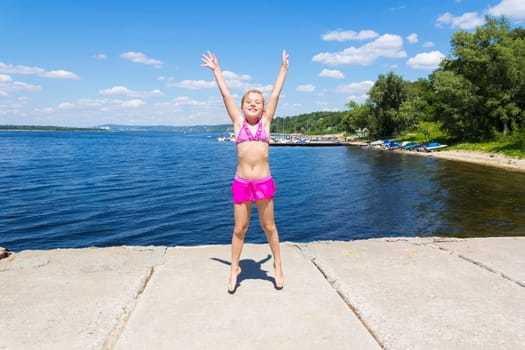 Jumping girl on the riverbank in pink swimsuit