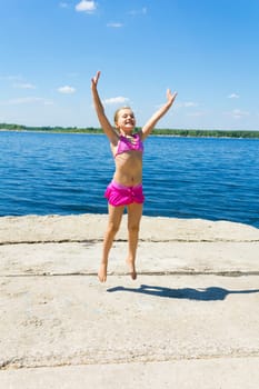 Jumping girl on the riverbank in pink swimsuit