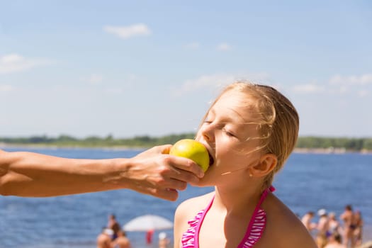 Photo of girl biting an apple from mother hand