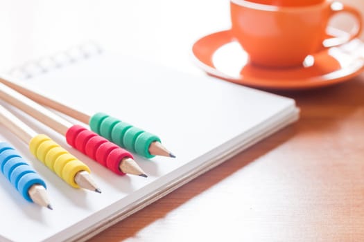 Pencils on open blank white notebook with coffee cup on the desk, stock photo
