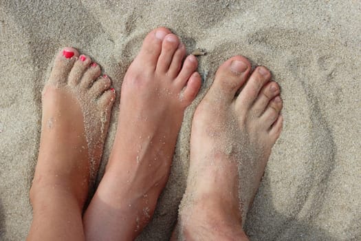 feet of father mother and their daughter stand on the sand
