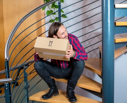 young man sitting in corridor and opening a package