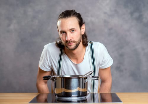 young bearded man with cooking pot in front of gray background