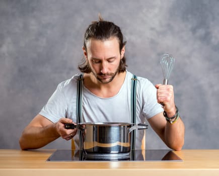 young bearded man with cooking pot in front of gray background