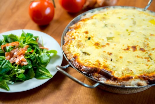baked quiche with field salad on wooden table