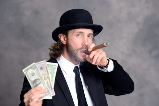 young businessman with bowler hat in black suit showing money and smoking big cigar