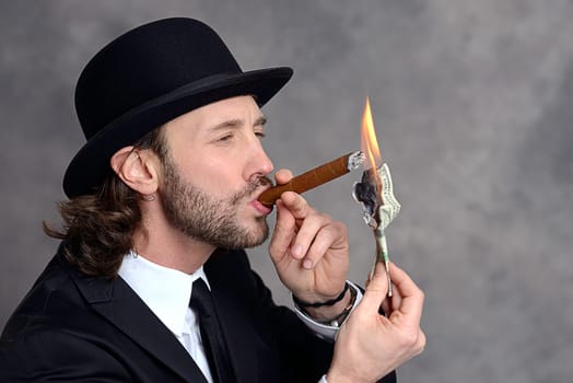young businessman with bowler hat lighting big cigar with money