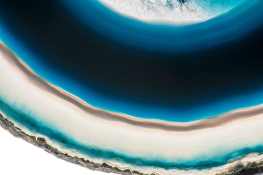 Close-up of a part of a flat,polished and transparent disc of an agate with round structures similar to the annual rings of a tree in blue and green with crusty edge insulated on white